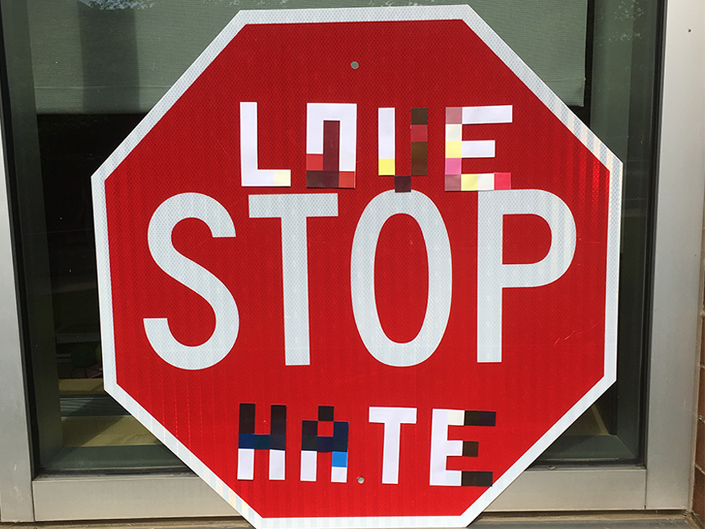 A stop sign with pixelated stickers spelling love and hate