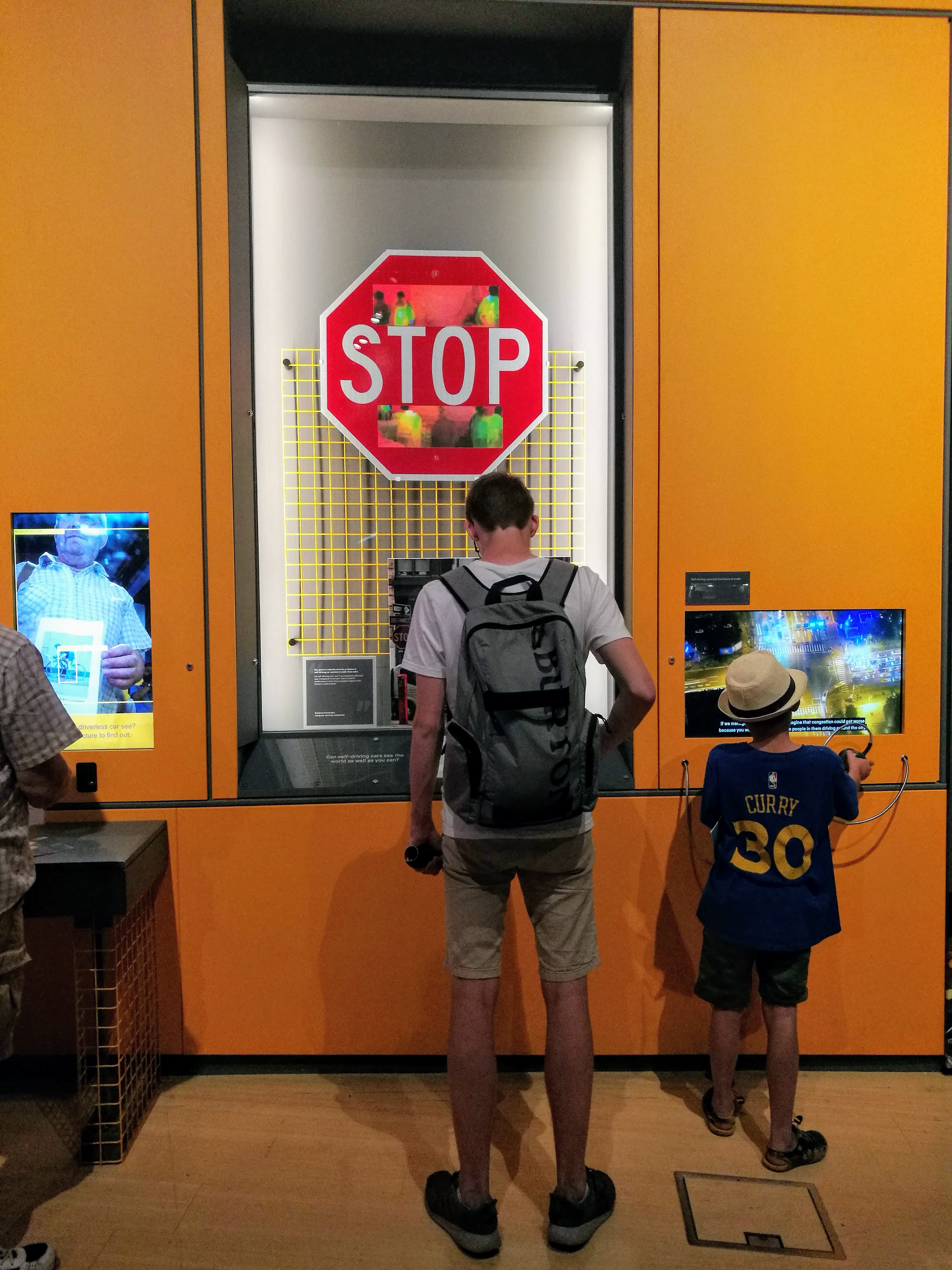 Visitors examine a display that shows a stop sign with stickers at the top and bottom of the sign.