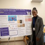 Ruth Nakigozi stands next to a posterboard highlighting her research project on oral histories